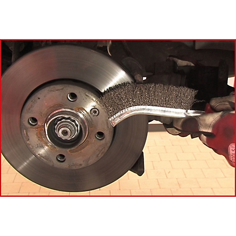 Nahaufnahme einer Autobremsanlage. Eine Hand, die einen Drahtbürstenpinsel hält, reinigt die Bremsscheibe.